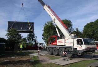 The crane lifts the classroom unit off the truck